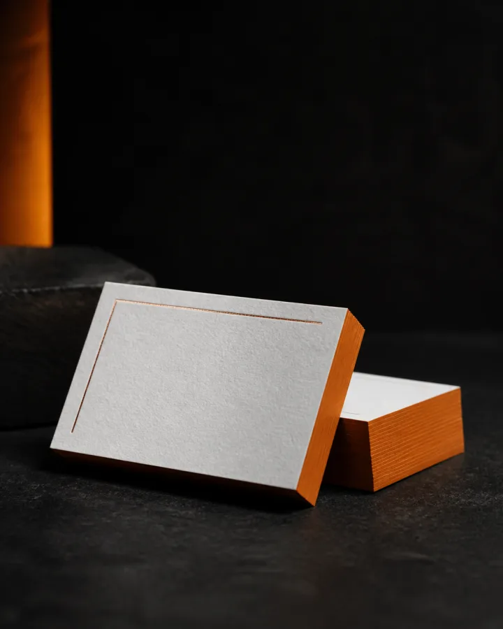 Illustrative white business cards with orange painted edges and a fine metallic detail